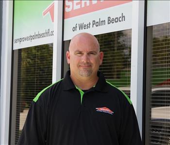 male employee in front of window with servpro logo smiling